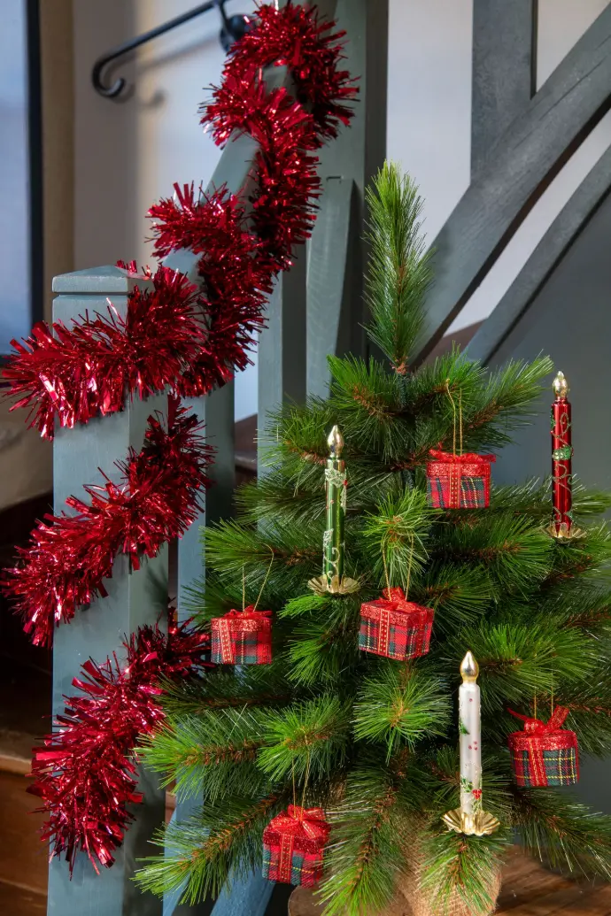 Sapin garni de boules et guirlande rouge au pied d’un escalier