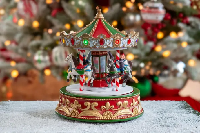 Carrousel de Noël décoratif rouge et doré devant un sapin illuminé